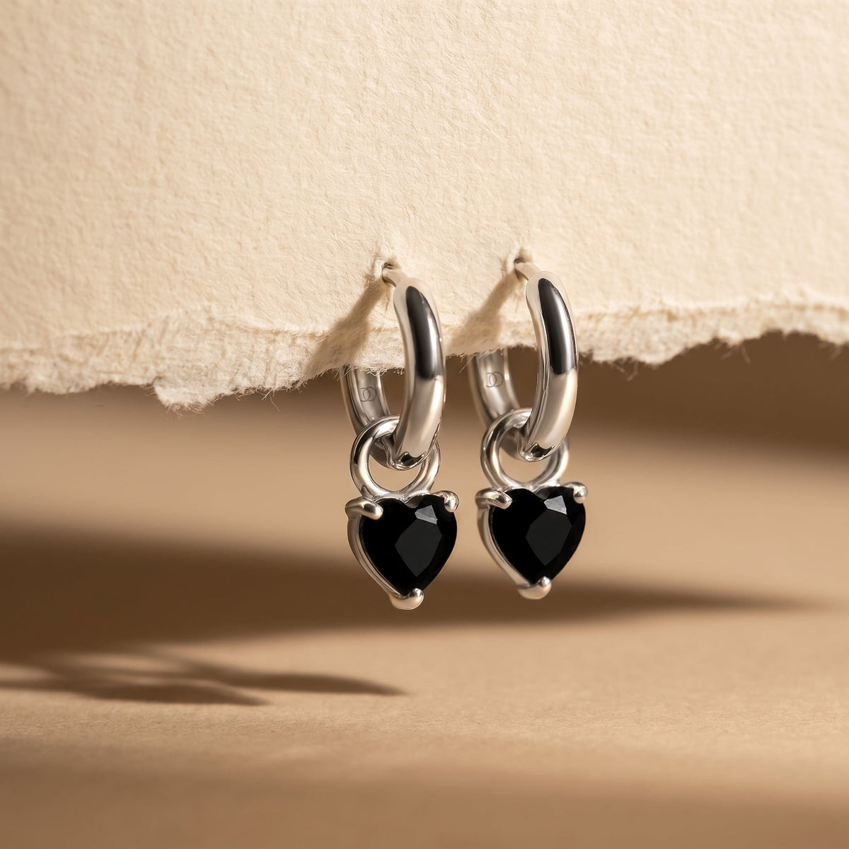Heart-shaped black obsidian hoops hanging against a sand-coloured wall