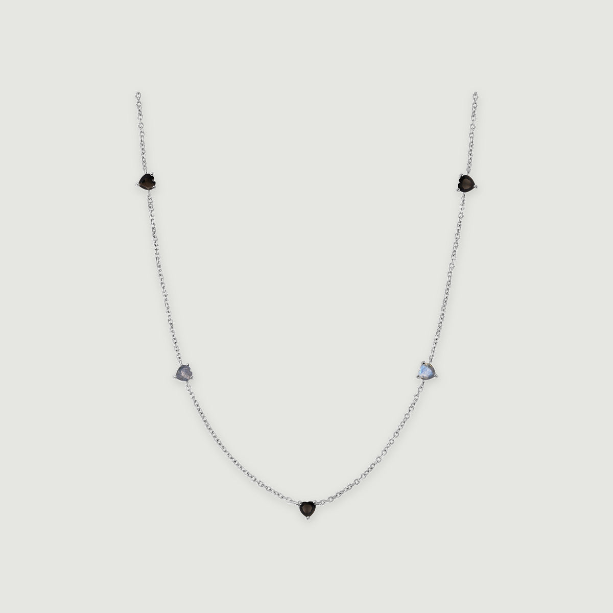 A silver chain curves around five small heart-shaped stones in black and blue-gray on a light gray surface.