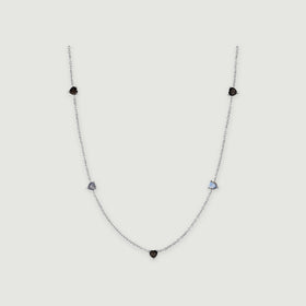 A silver chain curves around five small heart-shaped stones in black and blue-gray on a light gray surface.