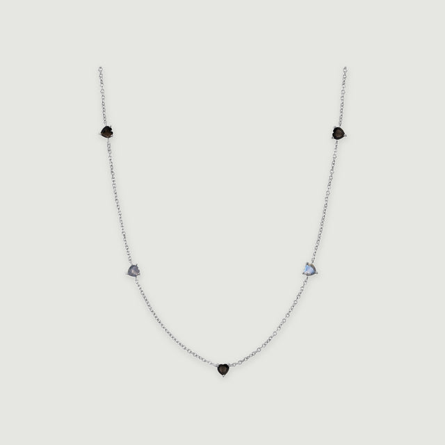 A silver chain curves around five small heart-shaped stones in black and blue-gray on a light gray surface.
