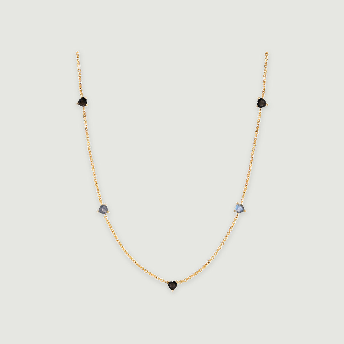 A yellow gold necklace has a central black heart and two pairs of heart-shaped stones along its curved chain.
