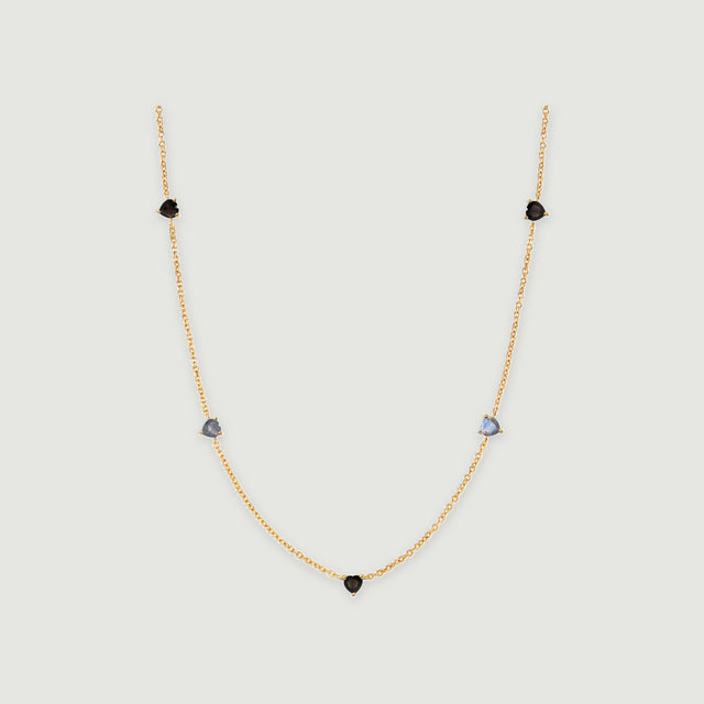 A yellow gold necklace has a central black heart and two pairs of heart-shaped stones along its curved chain.