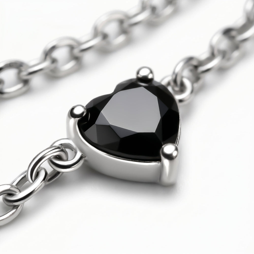 A faceted black heart is held by three silver prongs with oval chain links crossing the gray surface.