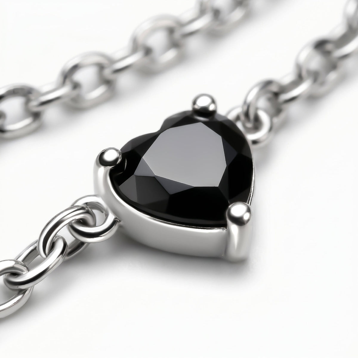 A faceted black heart is held by three silver prongs with oval chain links crossing the gray surface.