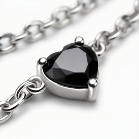 A faceted black heart is held by three silver prongs with oval chain links crossing the gray surface.