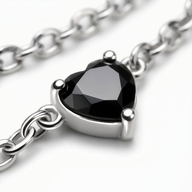 A faceted black heart is held by three silver prongs with oval chain links crossing the gray surface.