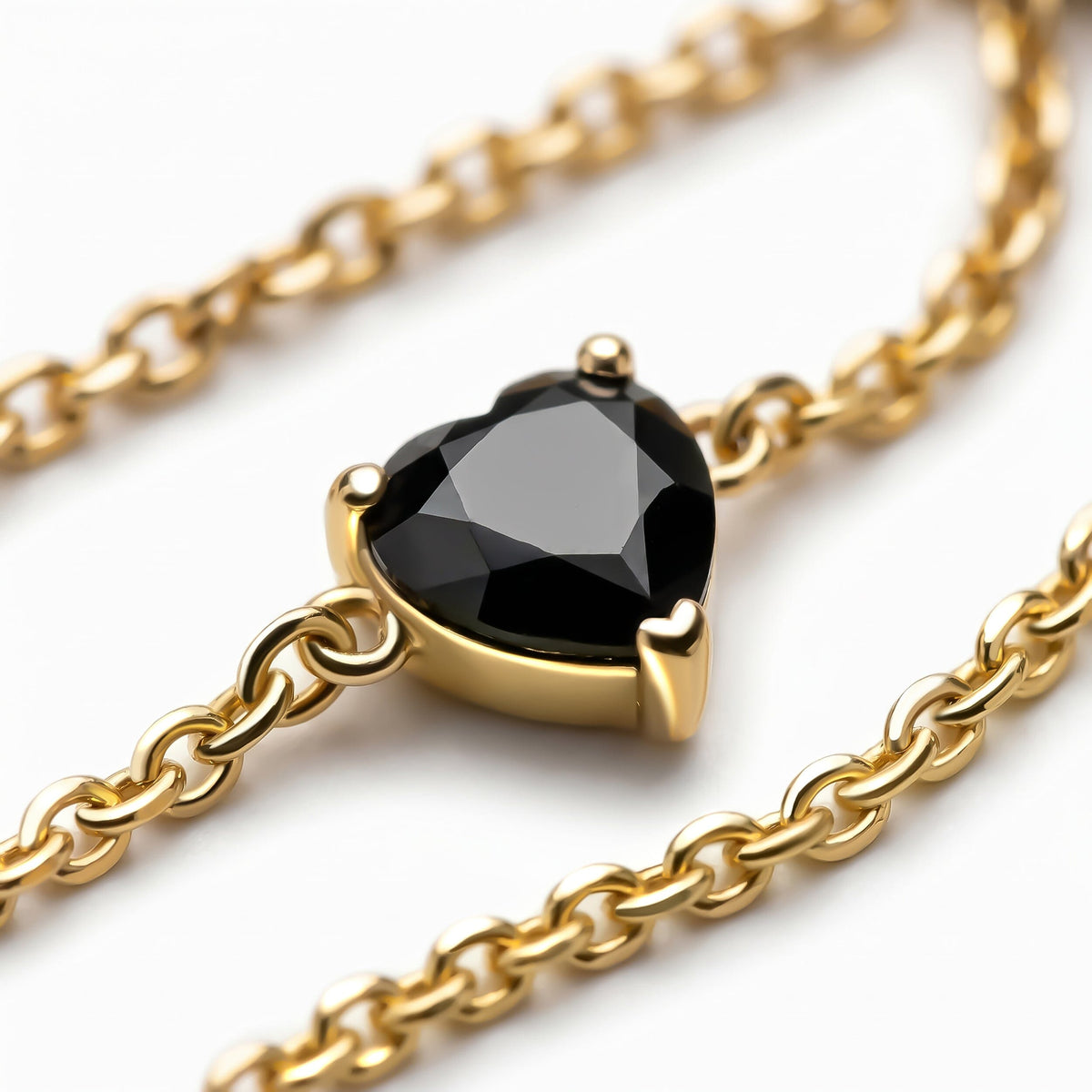 A polished yellow gold setting surrounds a black heart-shaped stone beside several curved chain links.