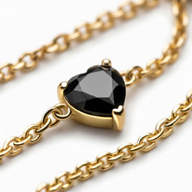 A polished yellow gold setting surrounds a black heart-shaped stone beside several curved chain links.