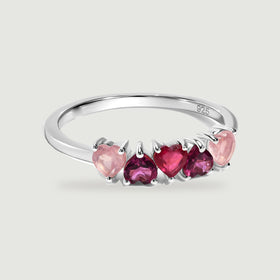 Five heart-shaped pink and raspberry stones sit across a polished silver ring against a soft gray background.