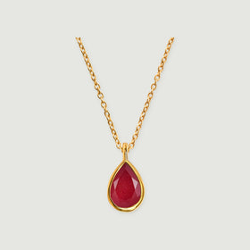 A yellow gold necklace with a faceted deep pink teardrop pendant is centered on a light gray background.