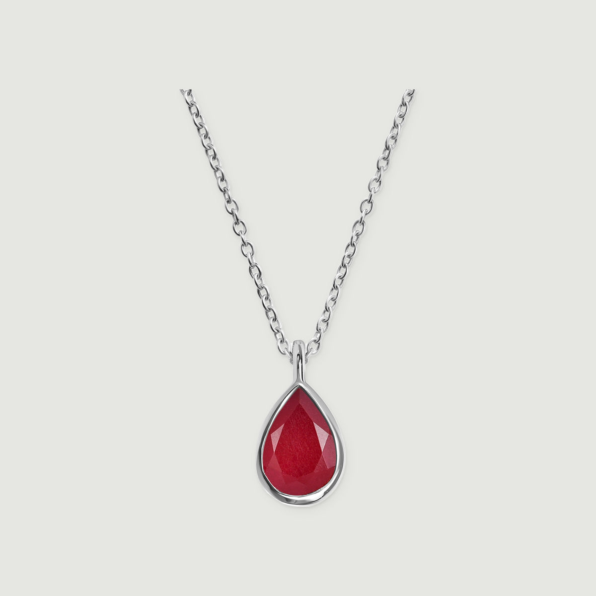A silver cable chain meets a polished bezel around a faceted pink teardrop stone on light gray.