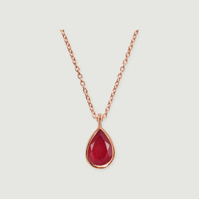 A rose gold chain and pear-shaped pink gemstone pendant are shown against a pale gray surface.