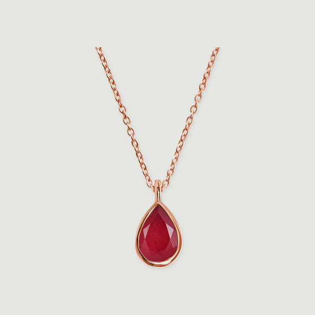 A rose gold chain and pear-shaped pink gemstone pendant are shown against a pale gray surface.