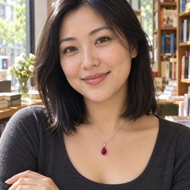 A woman with straight black hair wears a silver pink gemstone pendant and a charcoal top beside a bookshop window.