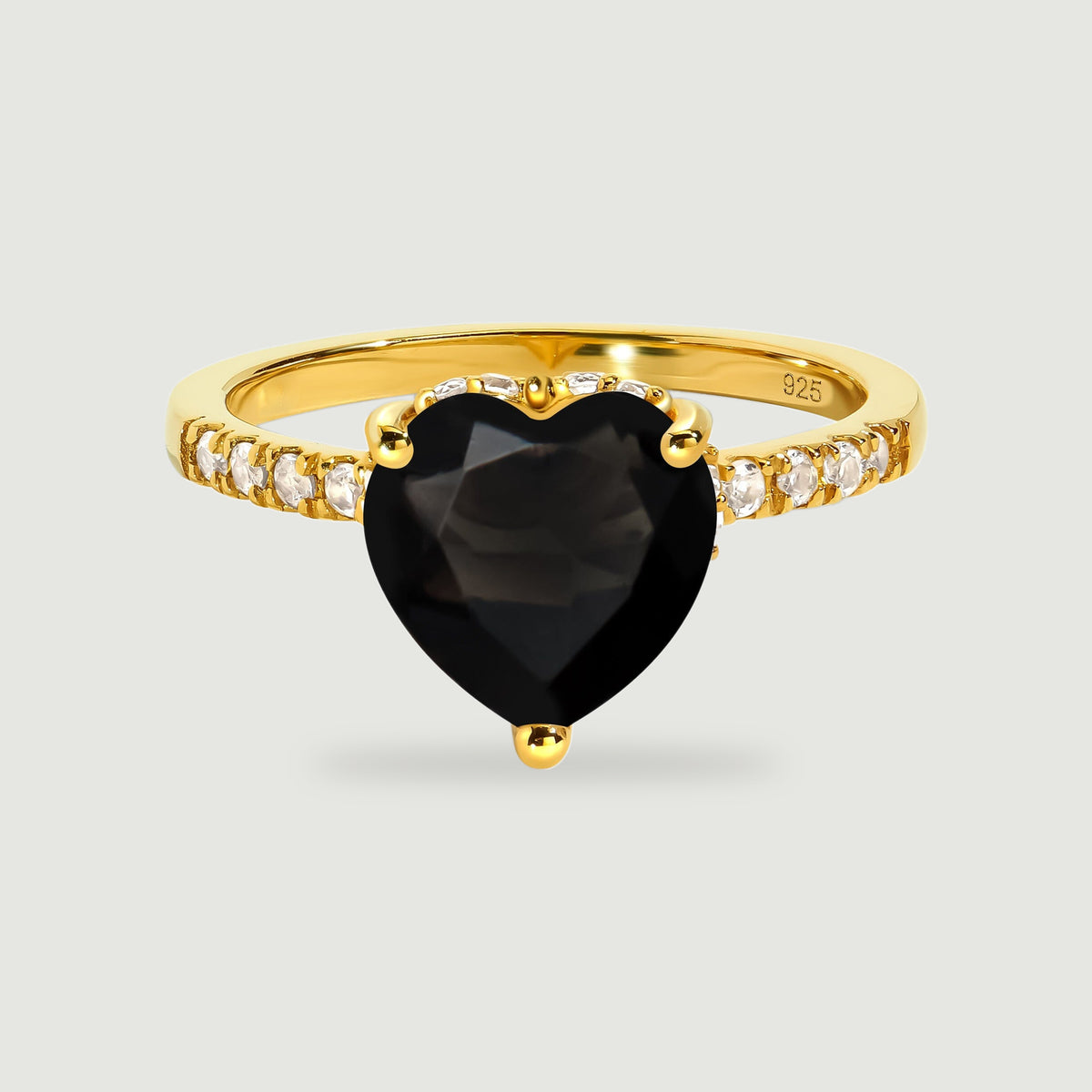A yellow gold vermeil ring with a black heart-shaped stone and clear stones along the band stands on pale gray.