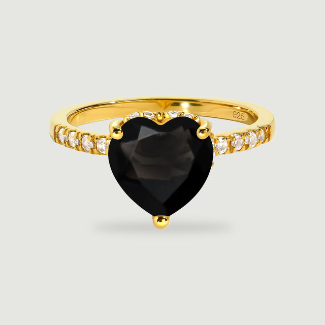 A yellow gold vermeil ring with a black heart-shaped stone and clear stones along the band stands on pale gray.