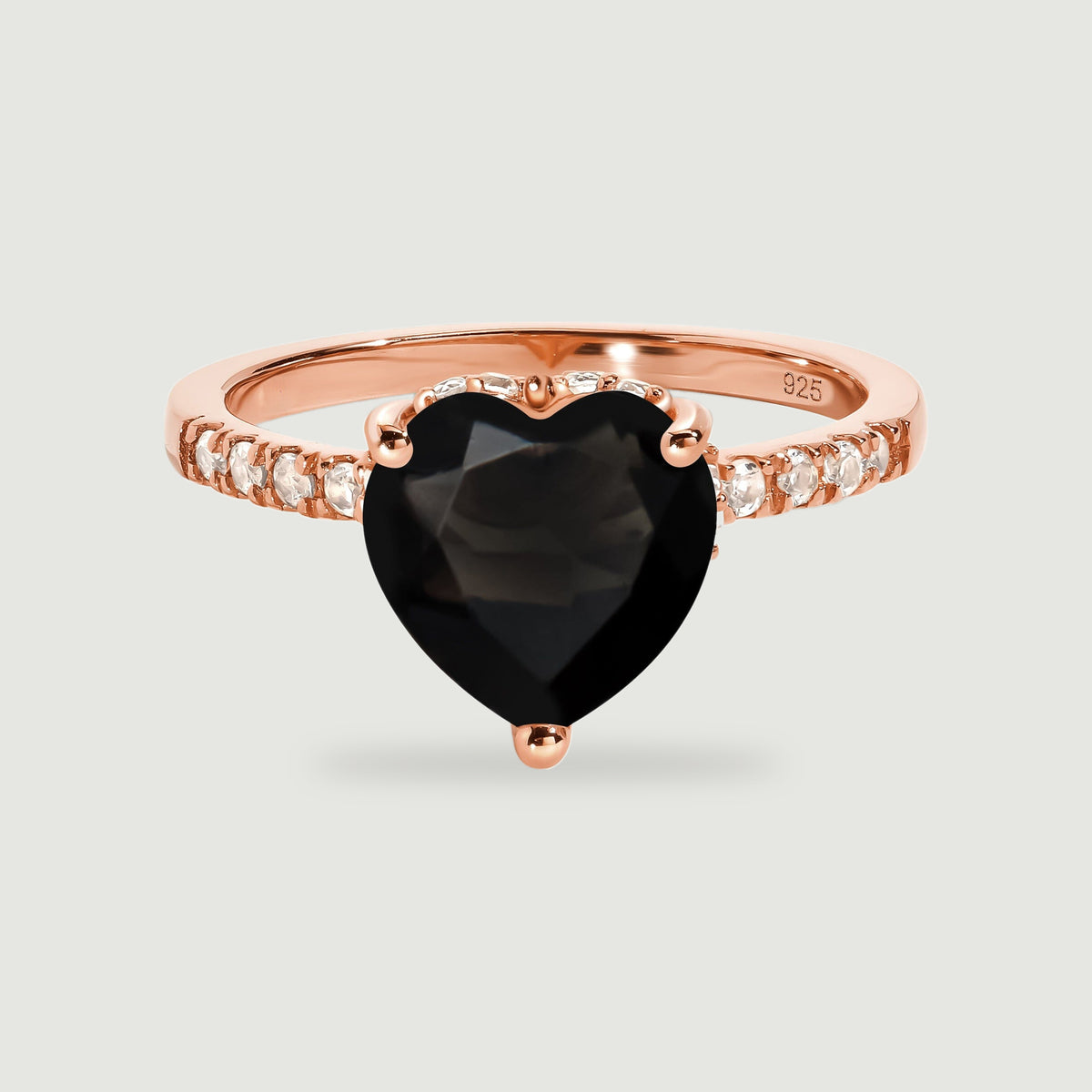 A rose gold vermeil ring presents a faceted black heart and a row of clear accent stones on pale gray.