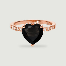 A rose gold vermeil ring presents a faceted black heart and a row of clear accent stones on pale gray.