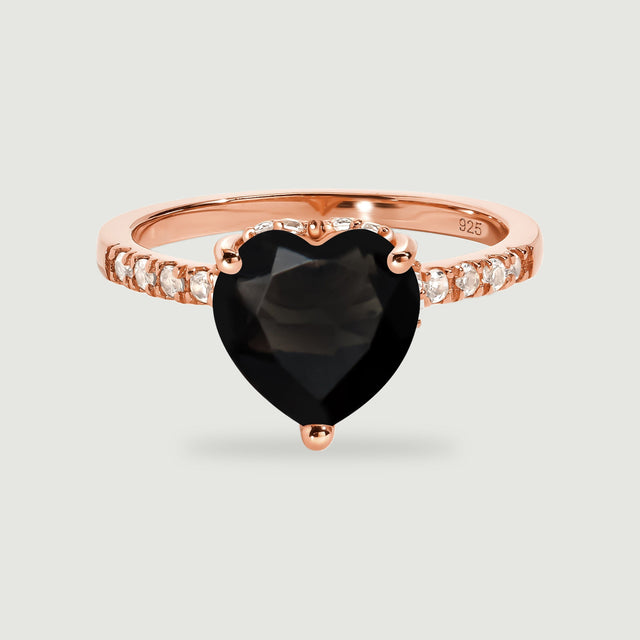 A rose gold vermeil ring presents a faceted black heart and a row of clear accent stones on pale gray.