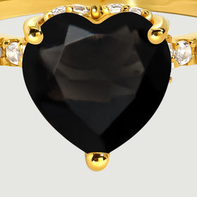 A close view shows the facets of a black heart-shaped stone held by yellow gold prongs beside clear accent stones.
