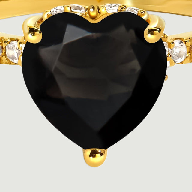 A close view shows the facets of a black heart-shaped stone held by yellow gold prongs beside clear accent stones.