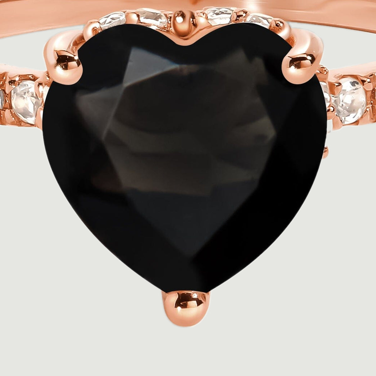 The black heart-shaped center stone fills this close-up, with rose gold prongs and clear stones visible at its sides.