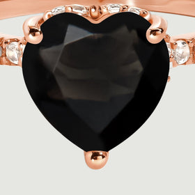 The black heart-shaped center stone fills this close-up, with rose gold prongs and clear stones visible at its sides.