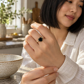 A woman wears a yellow gold vermeil black heart ring while adjusting a linen sleeve in a sunlit kitchen.