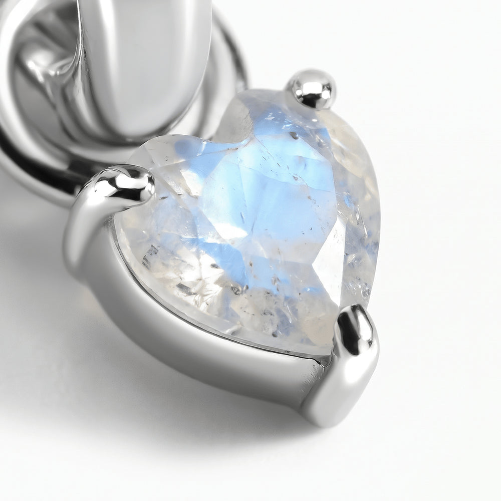 A close view shows blue reflections inside a heart-shaped moonstone held by silver-tone prongs.