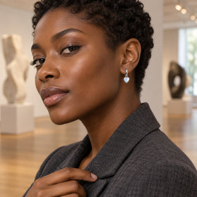 A woman with short coiled hair wears a silver-tone moonstone hoop earring in a sculpture gallery.