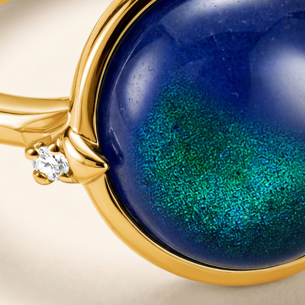 A close view shows the blue and teal cabochon beside a clear accent stone in a yellow gold setting.
