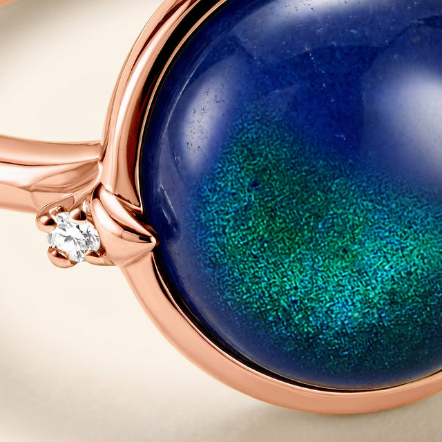 A glossy blue cabochon meets a small clear stone held by rose gold prongs in this close view.