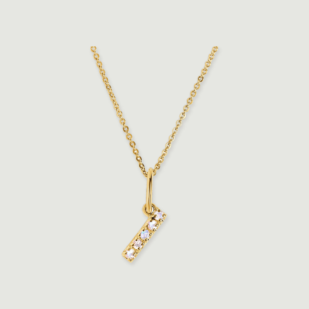 A gold-tone chain holds a slim I-shaped pendant set with five pale round stones against a light grey background.