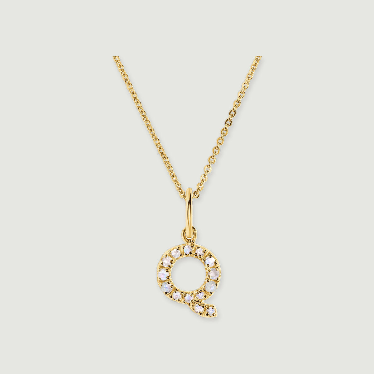 A circular Q-shaped pendant with pale faceted stones hangs from a polished gold-tone bail and fine chain.
