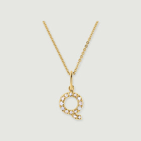 A circular Q-shaped pendant with pale faceted stones hangs from a polished gold-tone bail and fine chain.