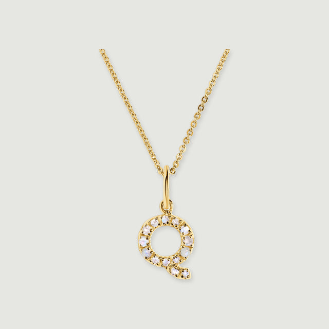 A circular Q-shaped pendant with pale faceted stones hangs from a polished gold-tone bail and fine chain.