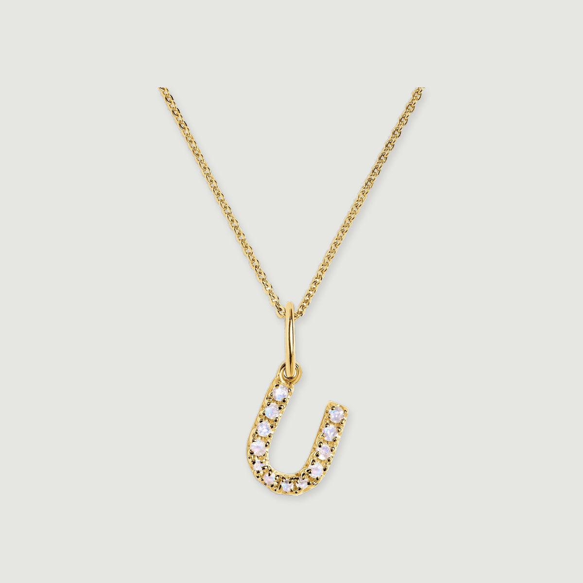 A gold-tone U pendant curves around a row of pale round stones below a delicate linked chain.