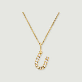 A gold-tone U pendant curves around a row of pale round stones below a delicate linked chain.