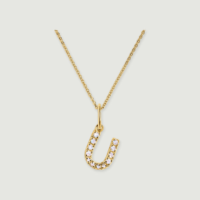 A gold-tone U pendant curves around a row of pale round stones below a delicate linked chain.