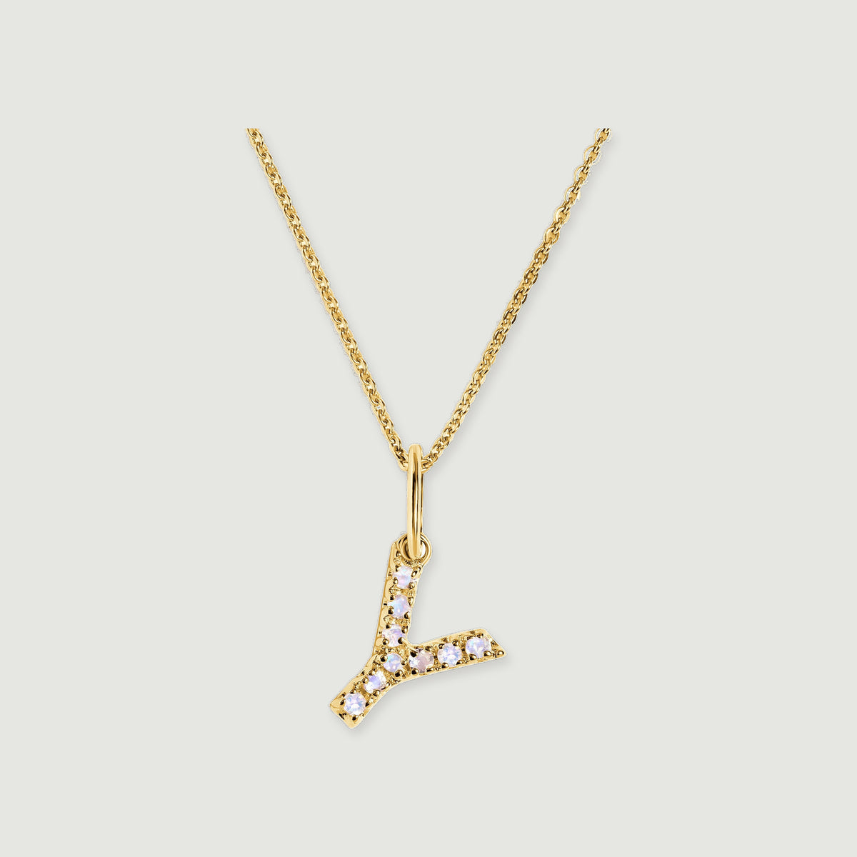 A branching Y-shaped pendant with pale round stones hangs from a gold-tone chain against light grey.