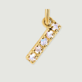 Five pale faceted stones sit in small gold-tone prongs along a narrow I-shaped charm in a close-up view.