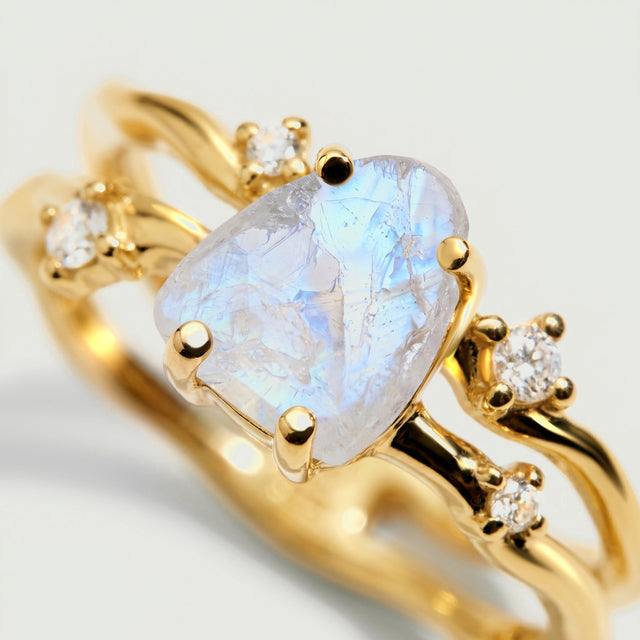 The yellow gold setting surrounds a translucent raw moonstone with rounded prongs and bright clear accent stones.