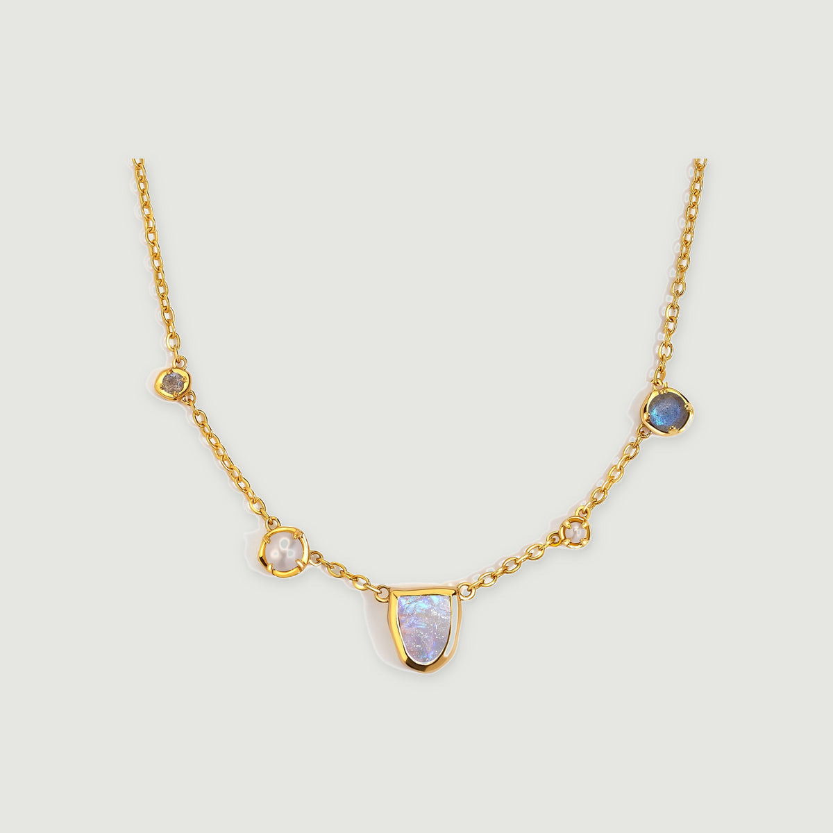 A gold-tone necklace has a shield-shaped moonstone center, two white pearls, and two round gray-blue stones.