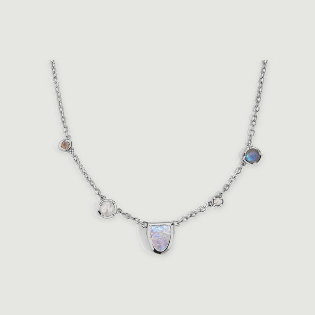 A silver-tone link necklace curves around a pale moonstone center with pearl and round stone accents.