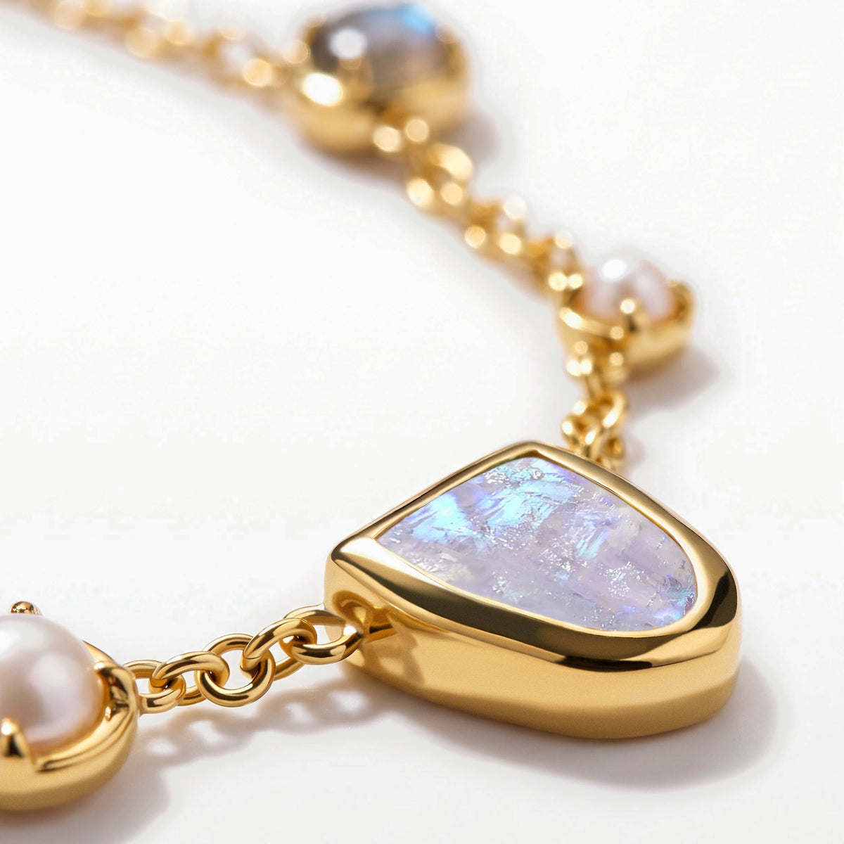 An angled close-up shows the raised gold-tone rim around the moonstone and adjoining oval chain links.