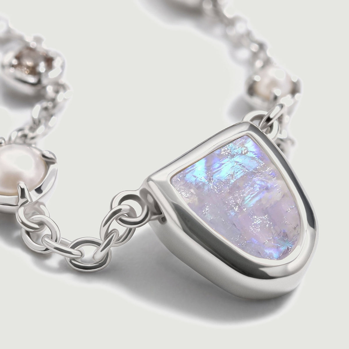 The silver-tone moonstone setting is shown from the side beside a pearl and polished chain links.