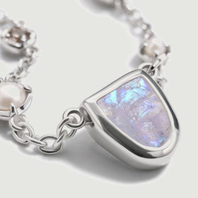 The silver-tone moonstone setting is shown from the side beside a pearl and polished chain links.