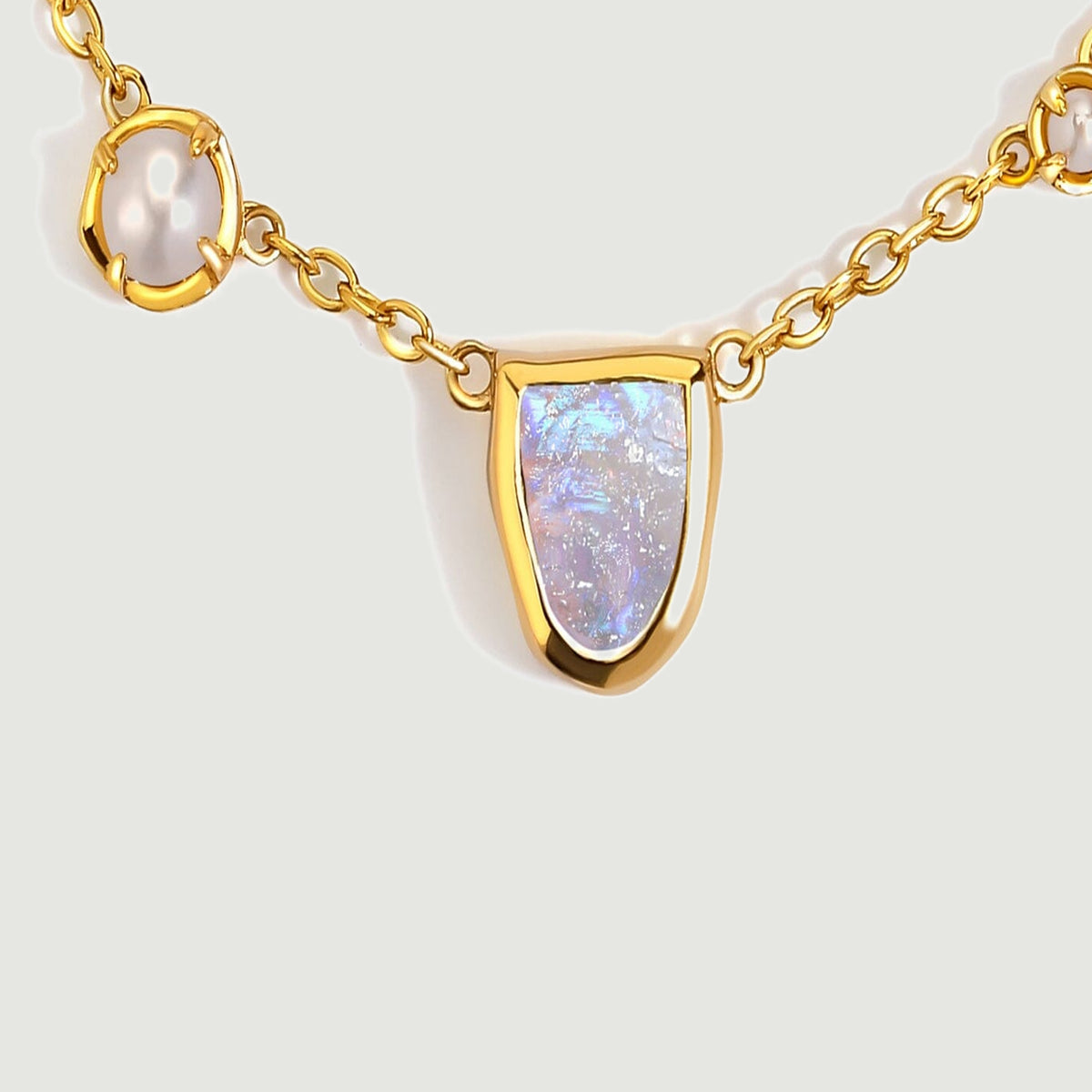 The gold-tone center section shows an iridescent moonstone between two white pearl accents.
