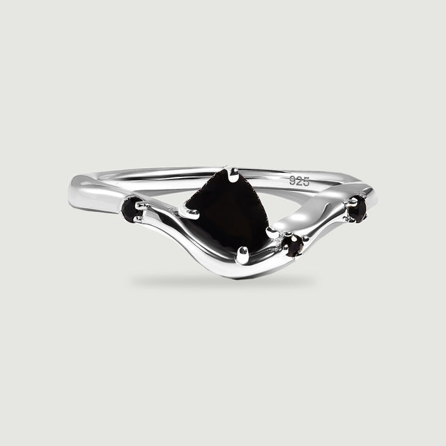 A sterling silver ring with a raw black center stone and three small black accents rests on a light gray surface.