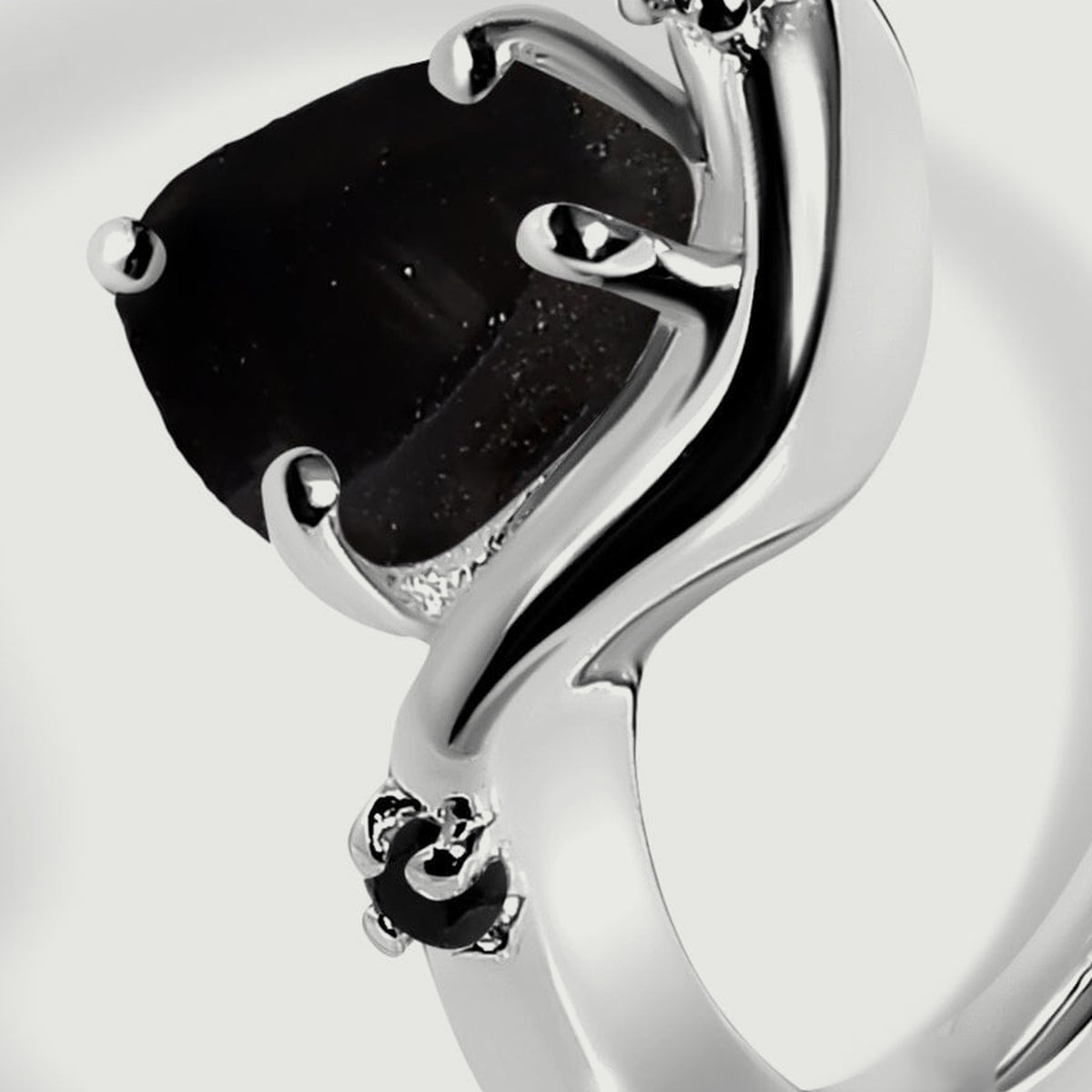 The side of the raw black stone shows an uneven surface beside polished silver and a small black accent.